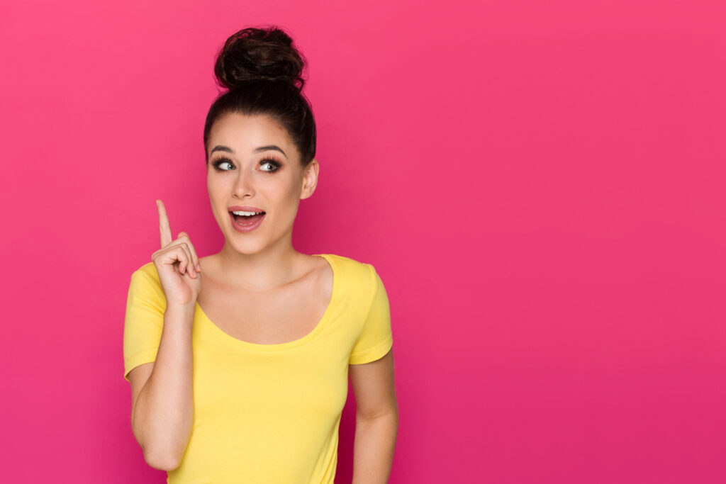 Young white woman wearing a yellow t-shirt against a pink backdrop expressing an idea