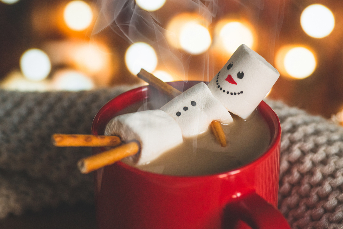 Marshmallow person floating in red holiday mug filled with hot chocolate