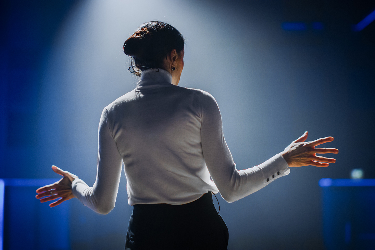 Young white woman in a spotlight presenting to a conference audience