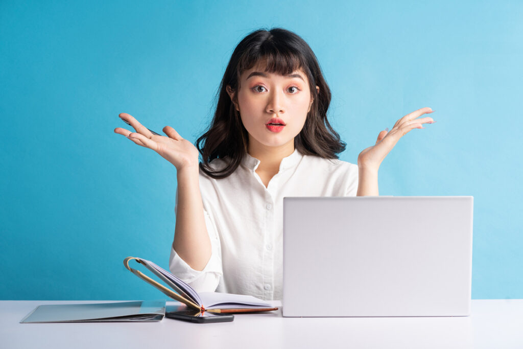 Young Asian woman in front of a laptop with hands in air trying to make a decision