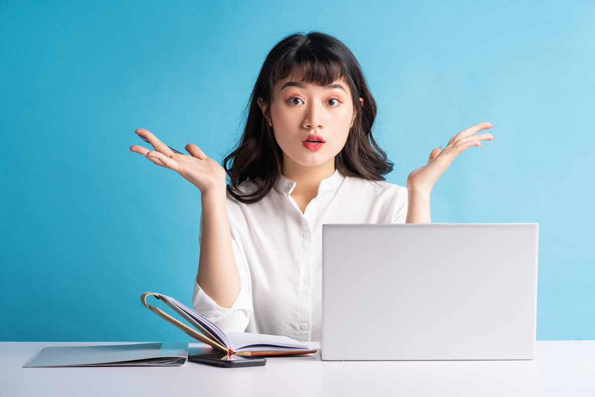 Young Asian woman in front of a laptop with hands in air trying to make a decision