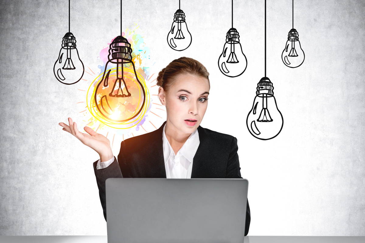 White, female thought leader in front of laptop with illustrated lightbulbs around her head