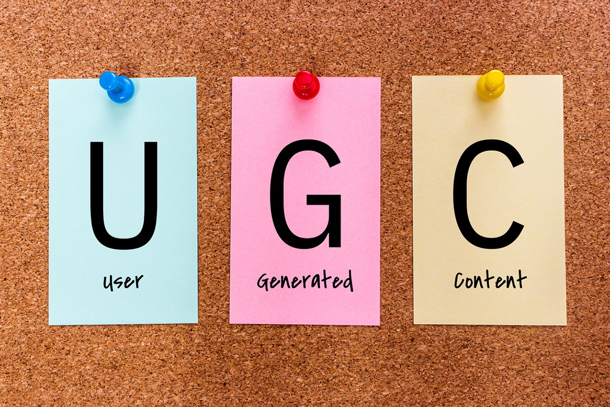 The letters UGC (User Generated Content) on multicolored stickers attached to a cork board.