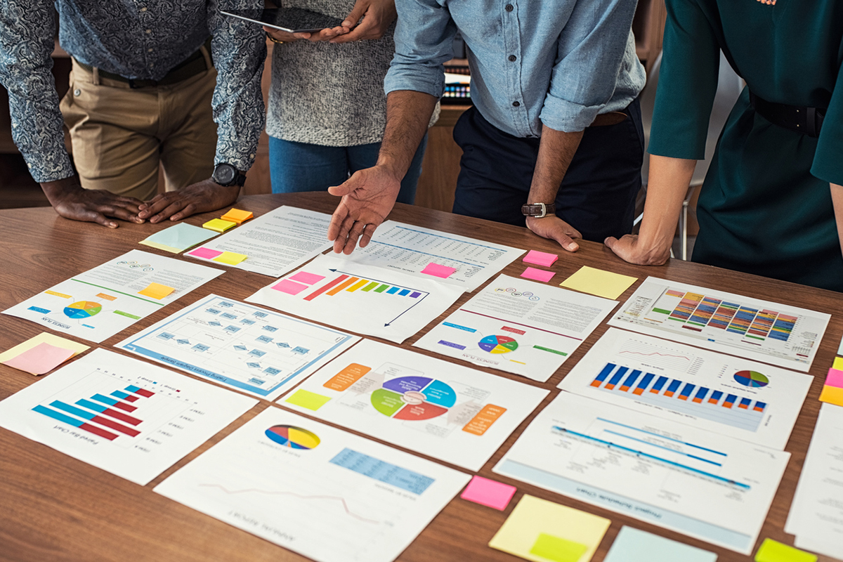 Charts, graphs, documents representing B2B marketing trends displayed on a table and people standing around the table