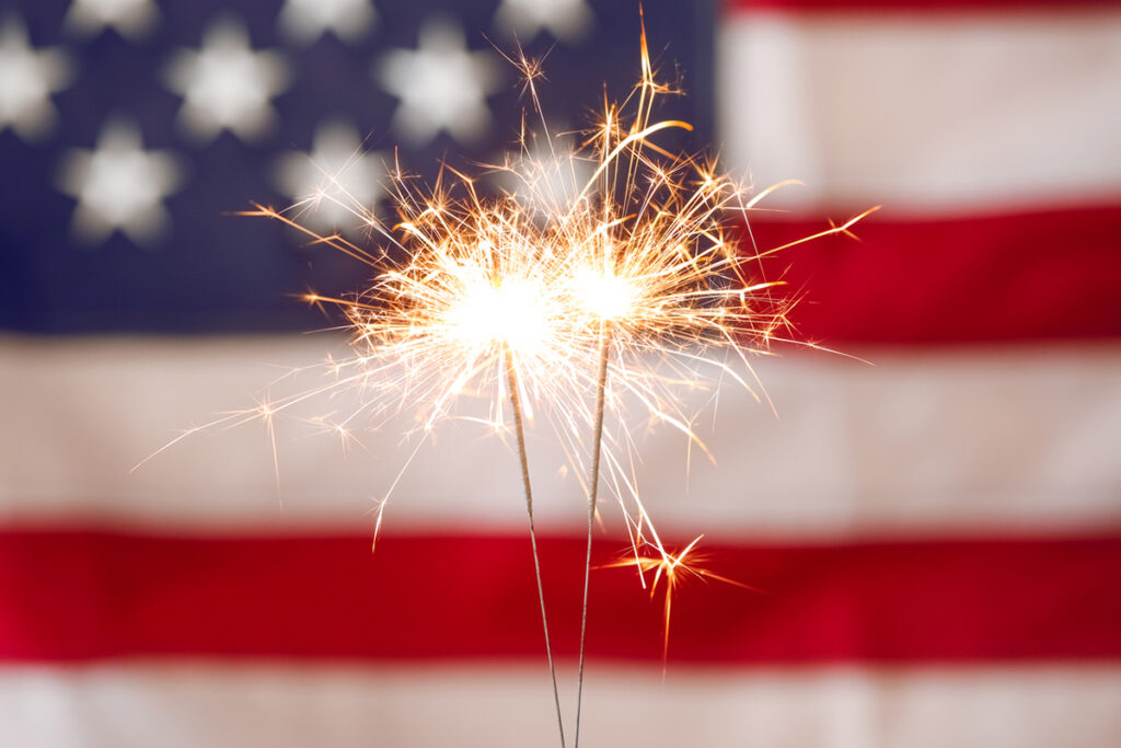 Freedom for Everyone -- Close up of 2 sparklers in front of an American flag