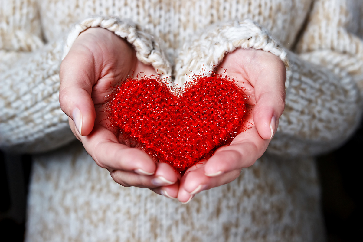 Girl in a light sweater gives a knitted heart.