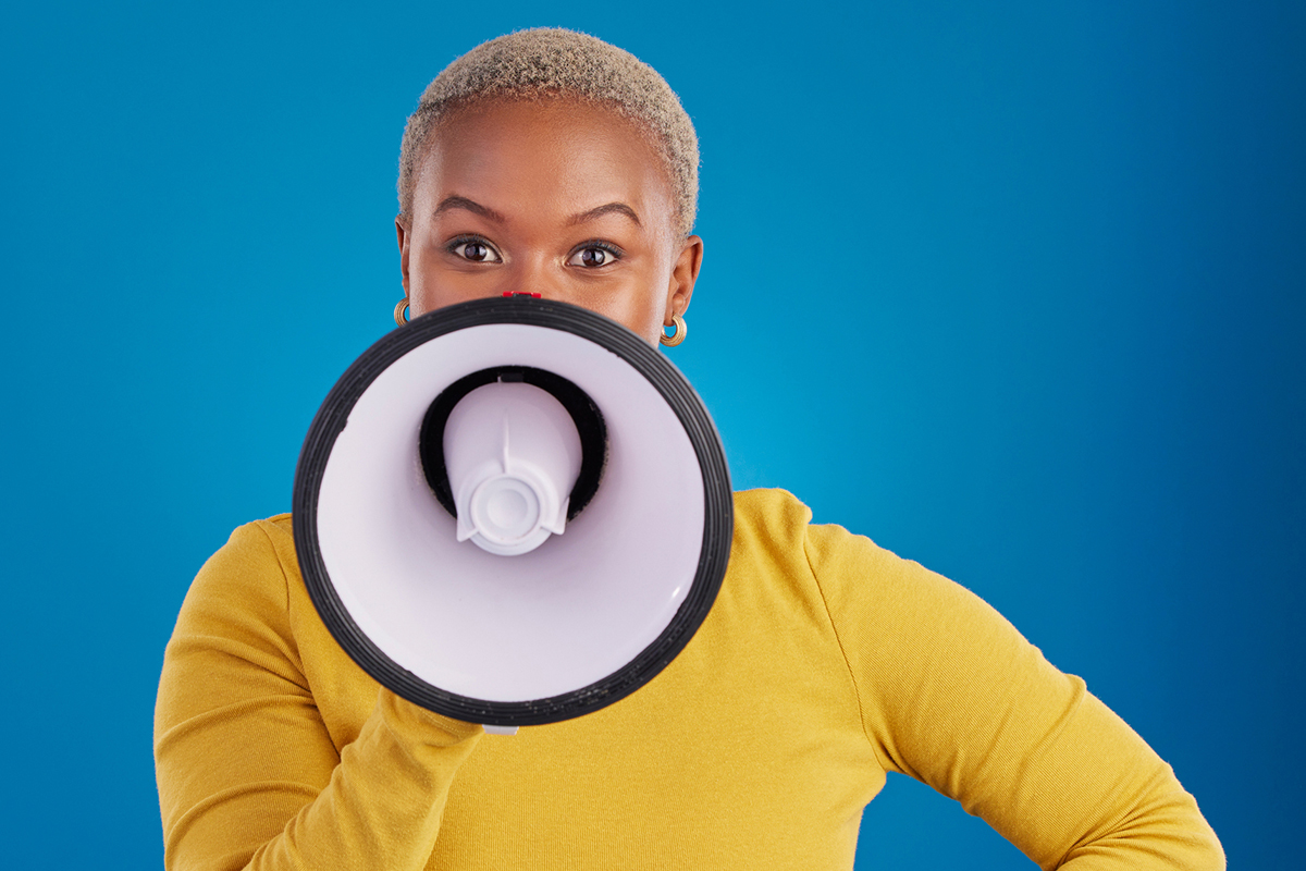 Black woman in yellow sweater holding megaphone against blue background
