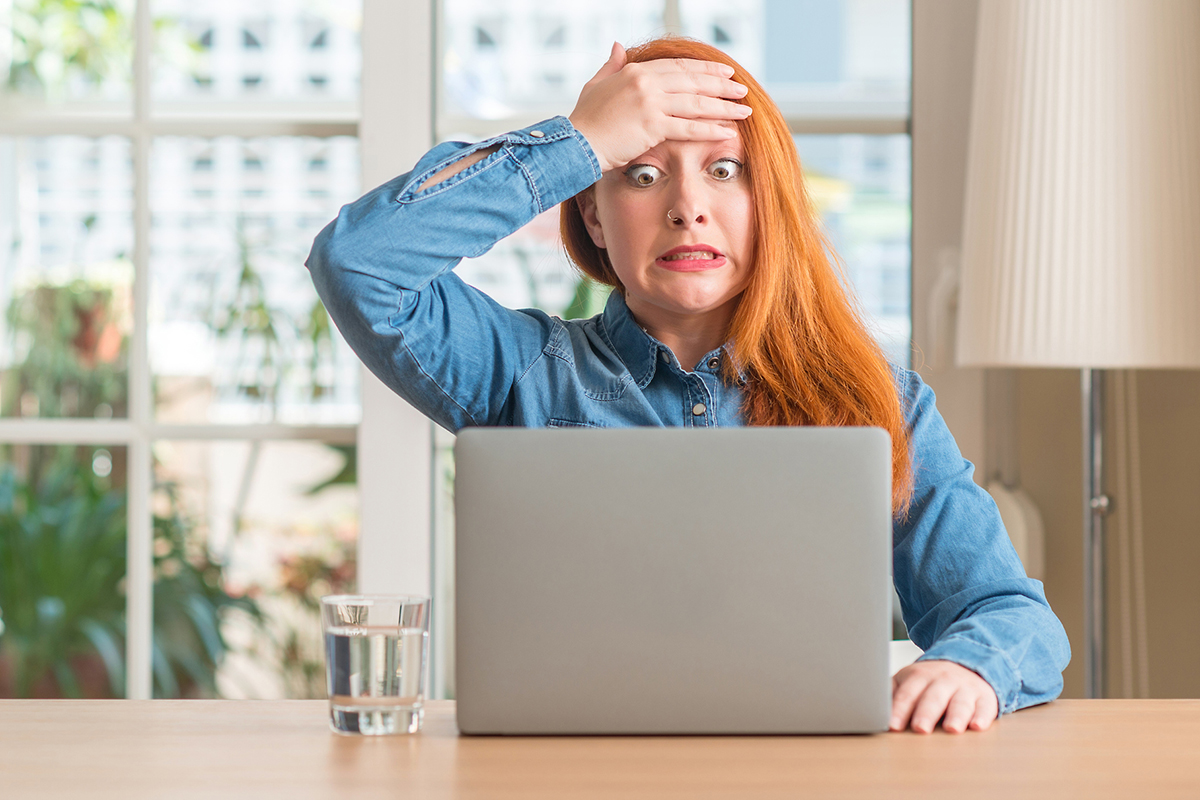 Young woman with red hair, looking at a laptop and reacting surprised to an unexpected event.