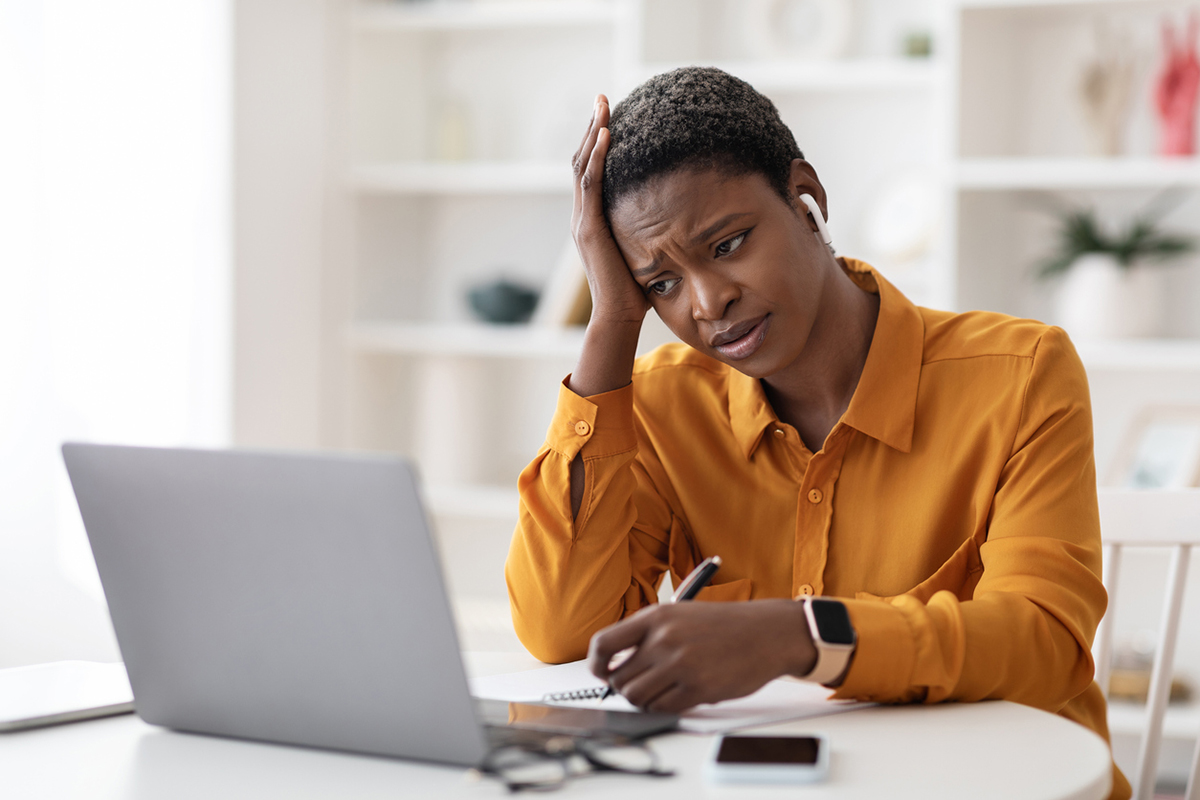 Black woman in an orange shirt looking at her laptop and unhappy with the training she is doing.