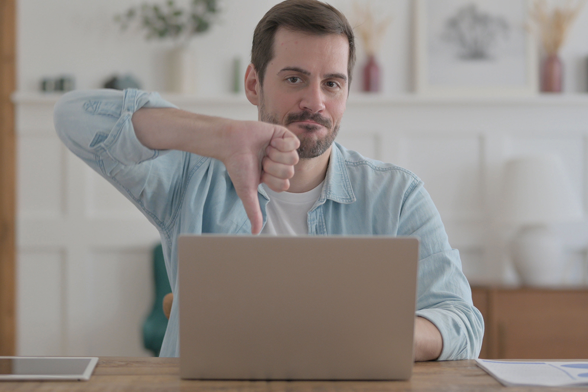 Young Man Showing Thumbs Down While using Laptop