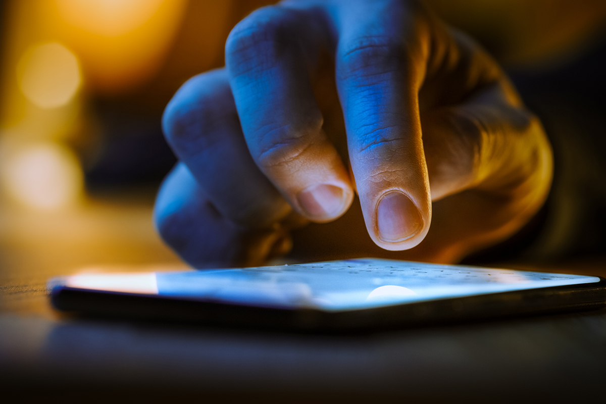 Close up of hand using a smart phone in the dark, representing dark social media communication
