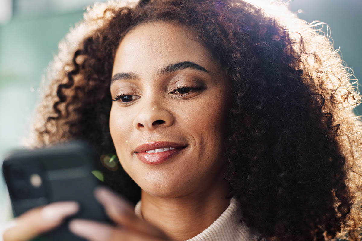 Young Black woman looking at a smartphone and smiling_illustrating how to re-engage past clients through non-spammy methods