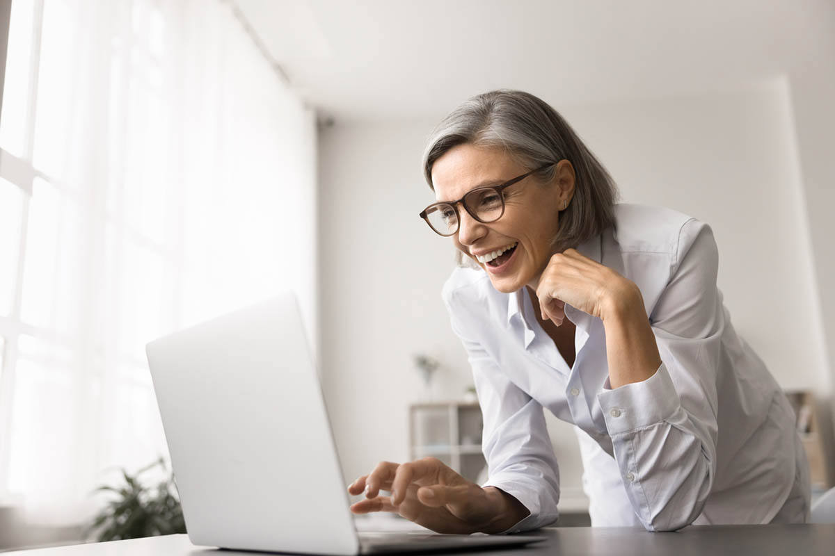 Mature businesswoman with glasses smiling and laughing at something she sees on a computer, illustrating the power of using humor in B2B marketing