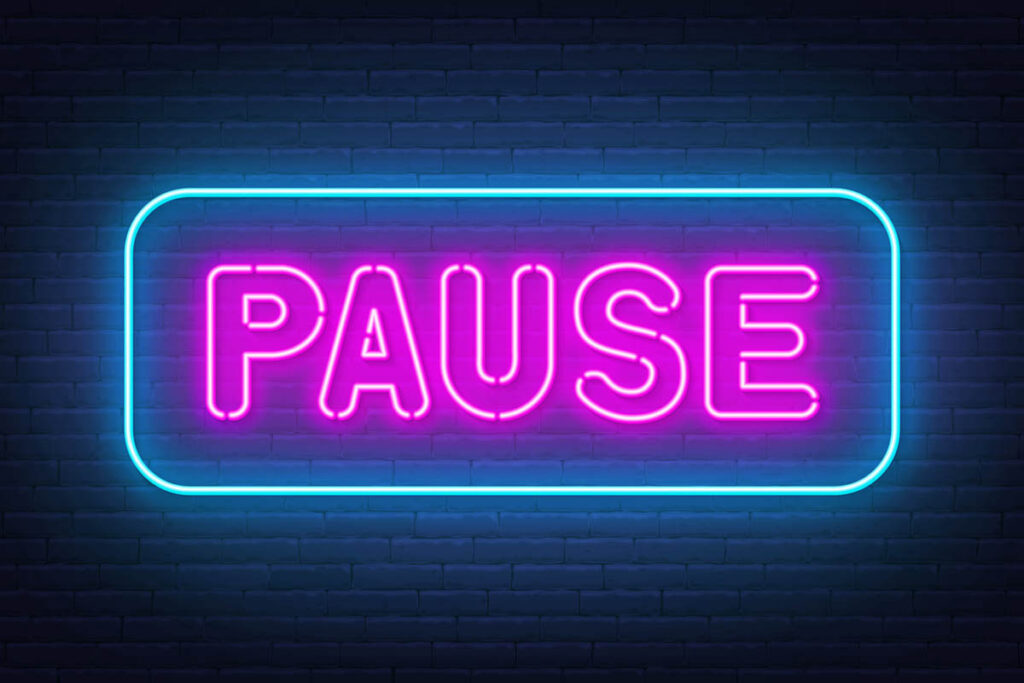 Neon sign with the word pause in pink on a black background, illustrating why people should pause before reacting