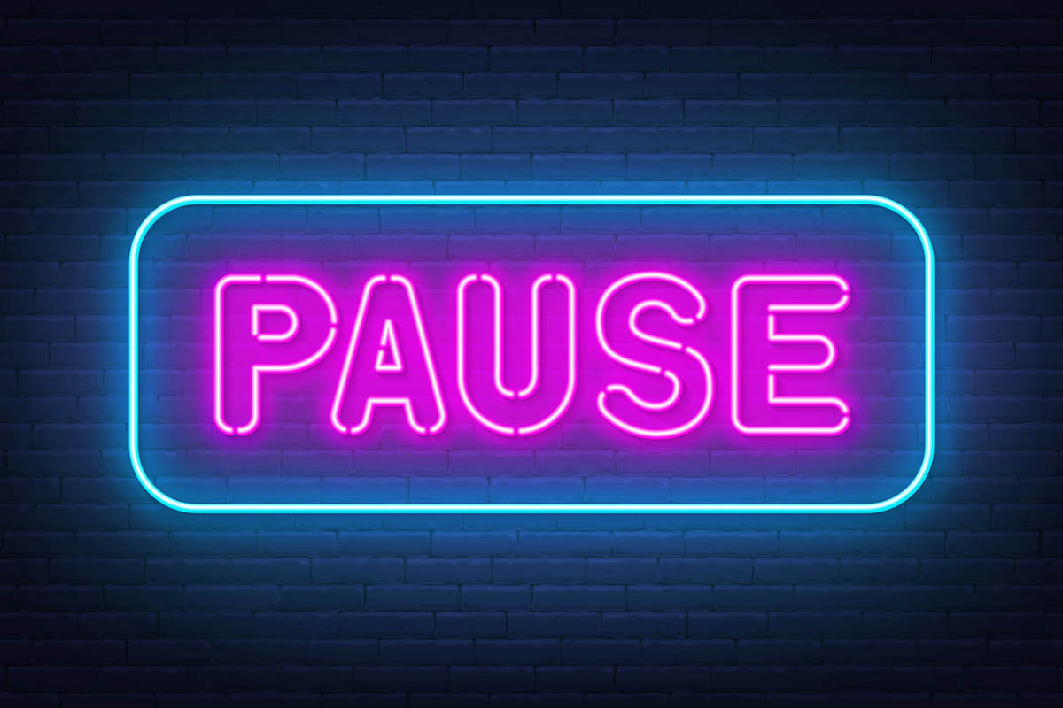 Neon sign with the word pause in pink on a black background, illustrating why people should pause before reacting