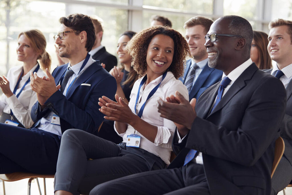 Smiling audience applauding at a B2B conference, illustrating how improving your B2B event speaker strategy makes for happy attendees