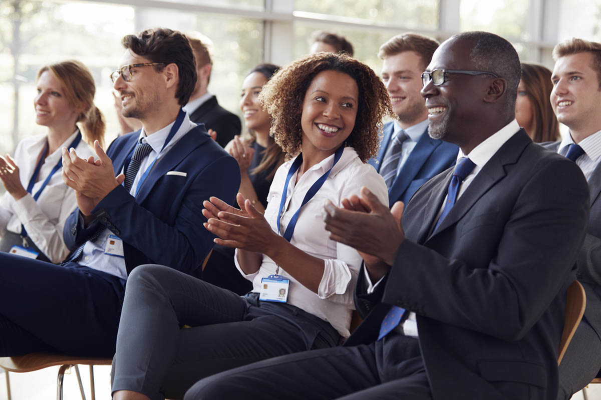 Smiling audience applauding at a B2B conference, illustrating how improving your B2B event speaker strategy makes for happy attendees