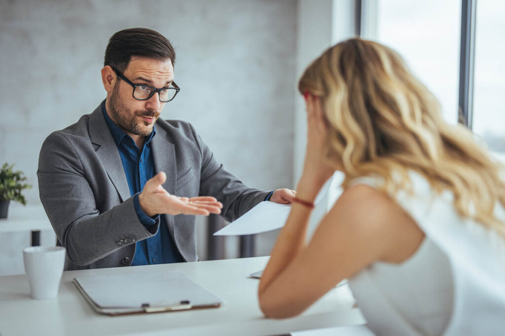 A man and woman in a business setting disagreeing over a document, illustrating how communication mistakes in the workplace create problems.