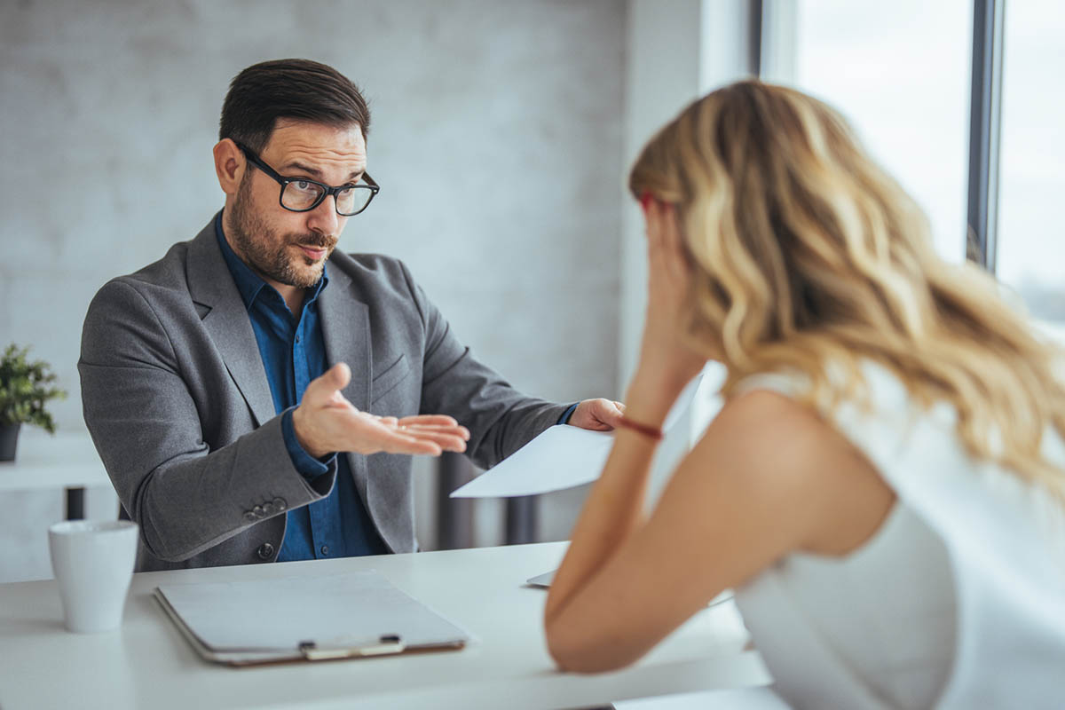 A man and woman in a business setting disagreeing over a document, illustrating how communication mistakes in the workplace create problems.