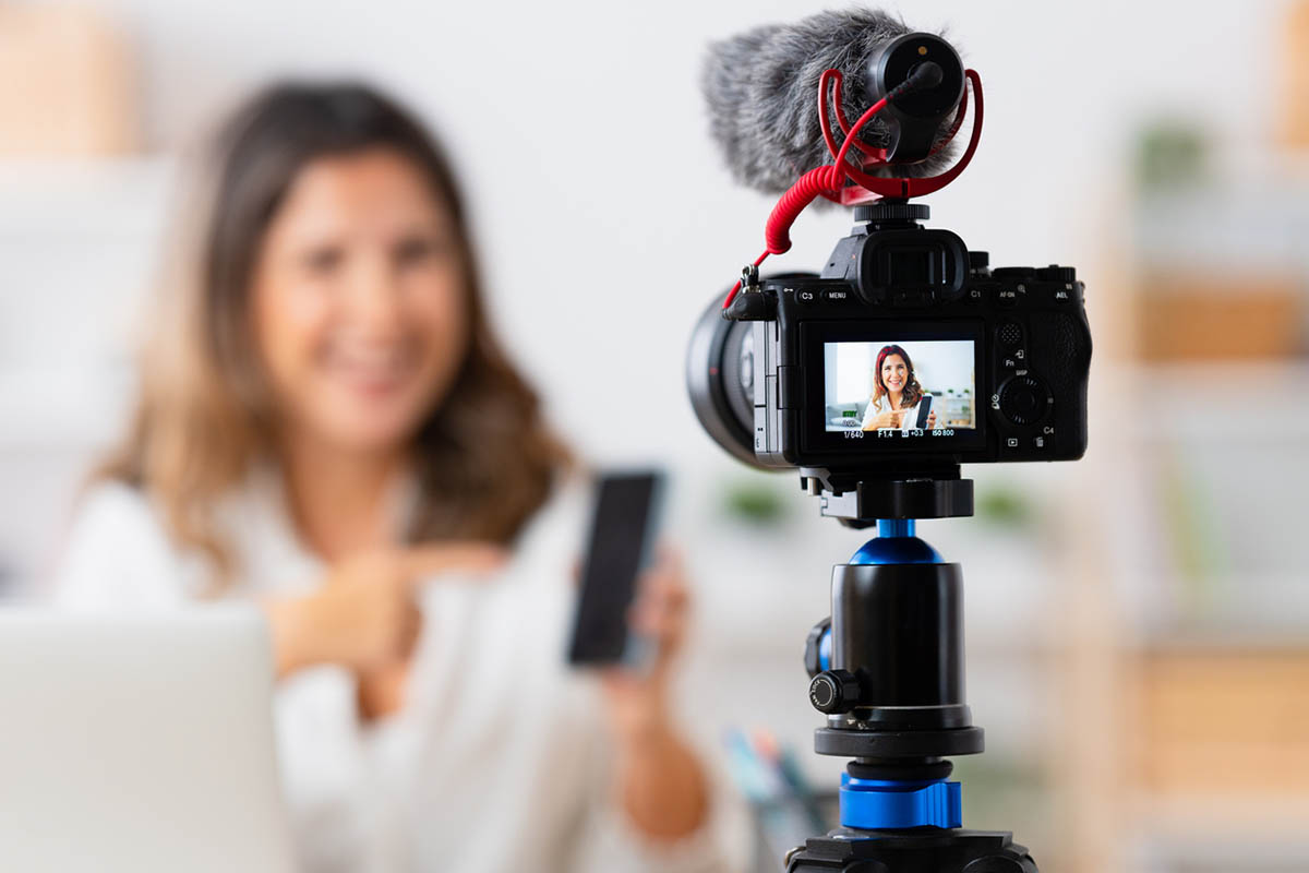 Woman recording a video, with the camera in front and the woman blurred in the background, illustrating the influence of content creators