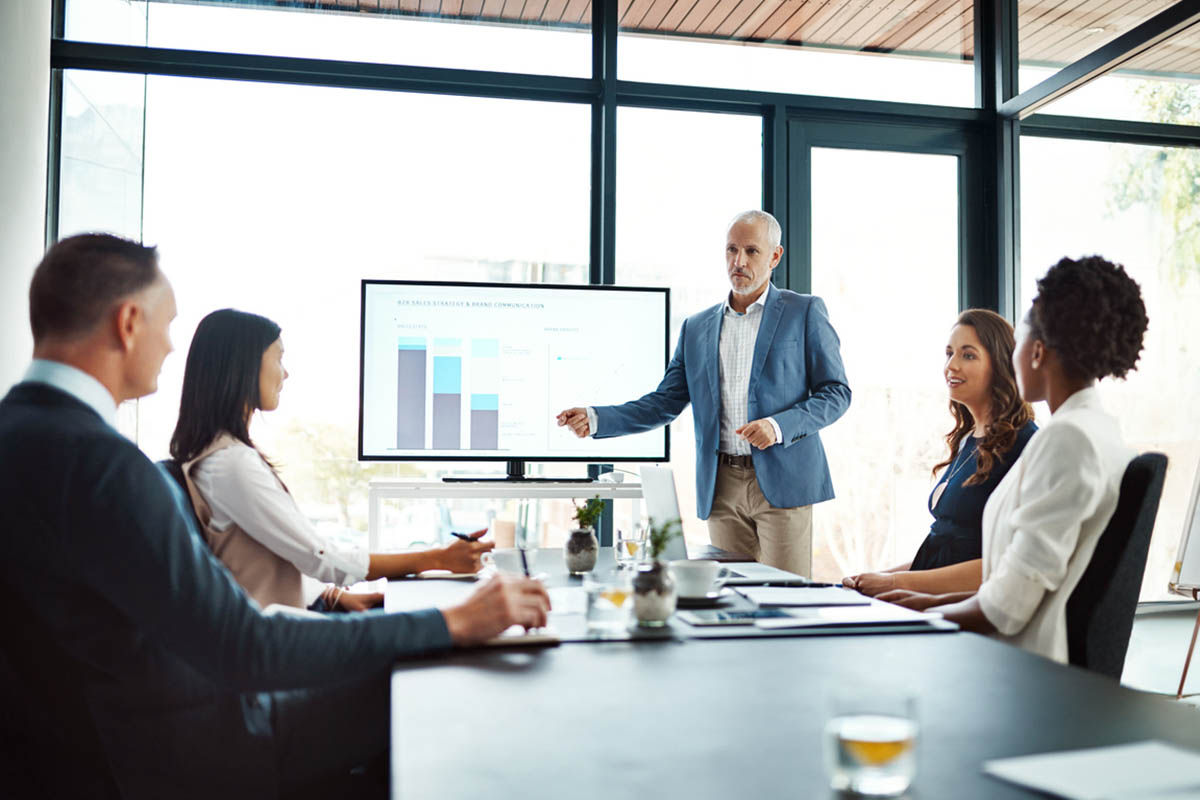 Business person pitching an idea to a group of executives, illustrating selling to the c-suite