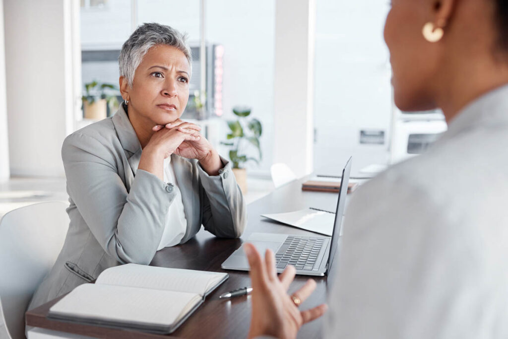 Older business woman talking with a dark-skinned younger woman about a project to ensure successful client outcomes