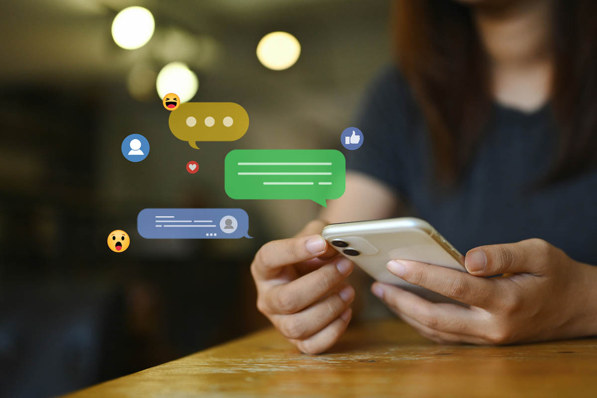 Young woman with dark hair looking at her smartphone, surrounded by floating emojis and comments, representing online reputation management on social media.