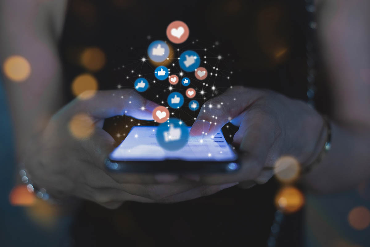 Hands holding a smartphone with floating social icons, illustrating how interaction and feedback shape an effective social media engagement strategy.