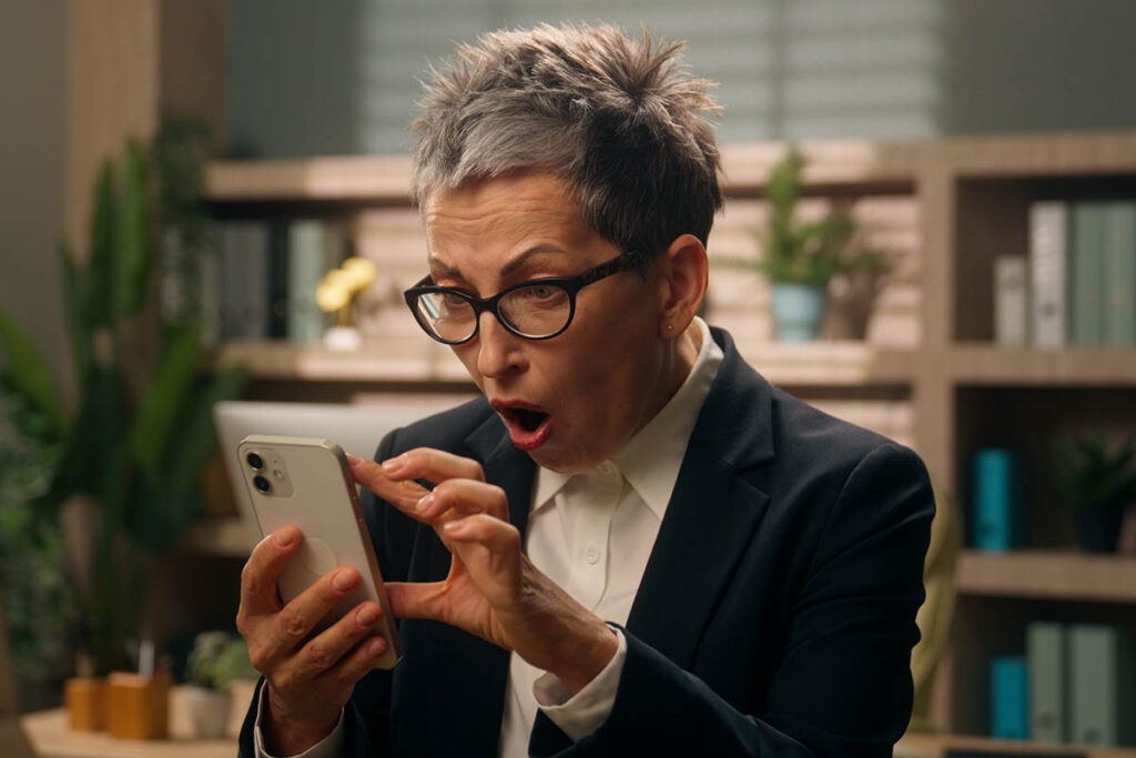 Older white woman with short hair and looking shocked at her smartphone, illustrating how social media posts can risk alienating your buyers and damaging trust.