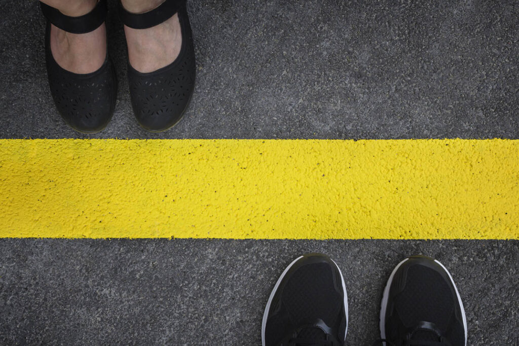 Top-down view of two people standing on opposite sides of a bold yellow line on pavement, illustrating how to set client boundaries and maintain clear separation.