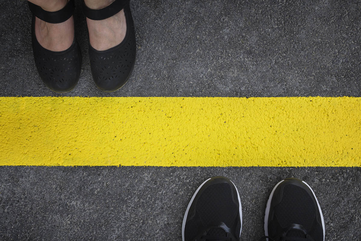 Top-down view of two people standing on opposite sides of a bold yellow line on pavement, illustrating how to set client boundaries and maintain clear separation.