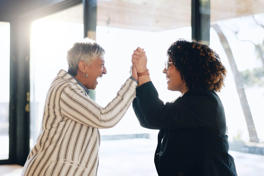 Two professionals celebrate and encourage each other in a workplace setting, illustrating how meaningful support can help people navigate disruption through practical encouragement and human connection.