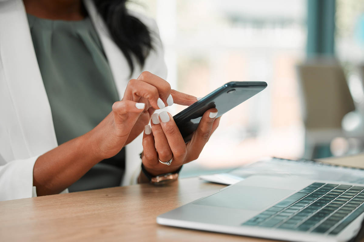 A professional uses a smartphone while working at a laptop, illustrating how creating a consistent content experience across digital platforms helps build audience engagement and encourages repeat interaction with social media content.