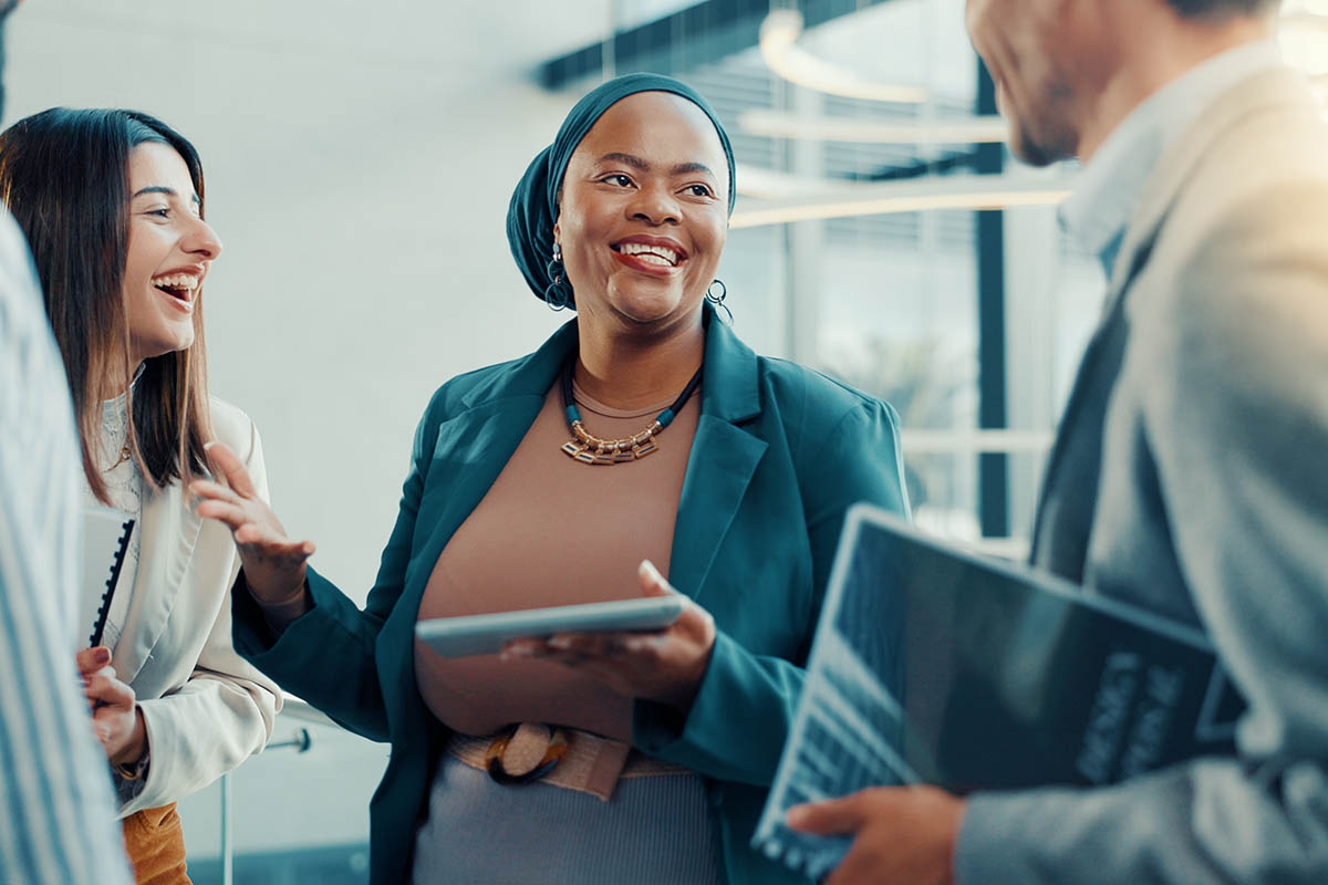 Three business professionals smile and chat in a relaxed office setting, illustrating how low-pressure sales create welcoming buying experiences by encouraging genuine conversations instead of high-pressure sales tactics.