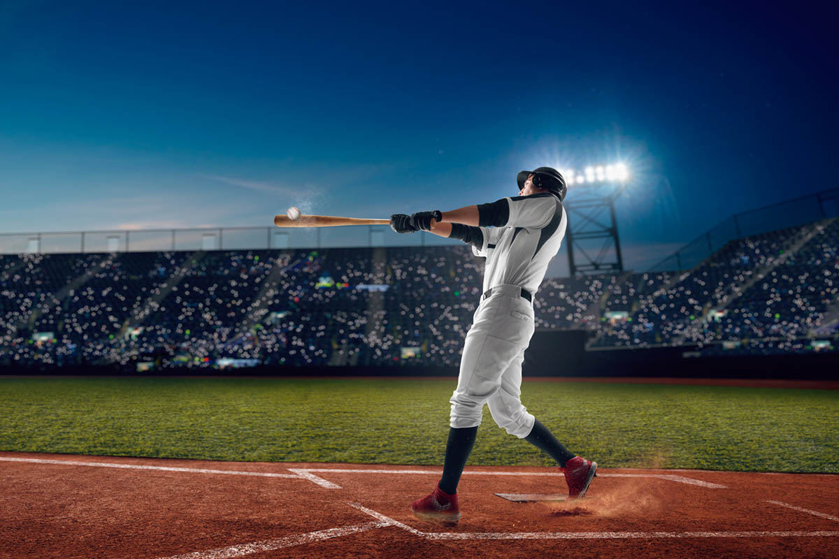 Baseball player follows through on a powerful swing after making contact with the ball during a night game, illustrating the confidence and commitment behind swinging for the fences.