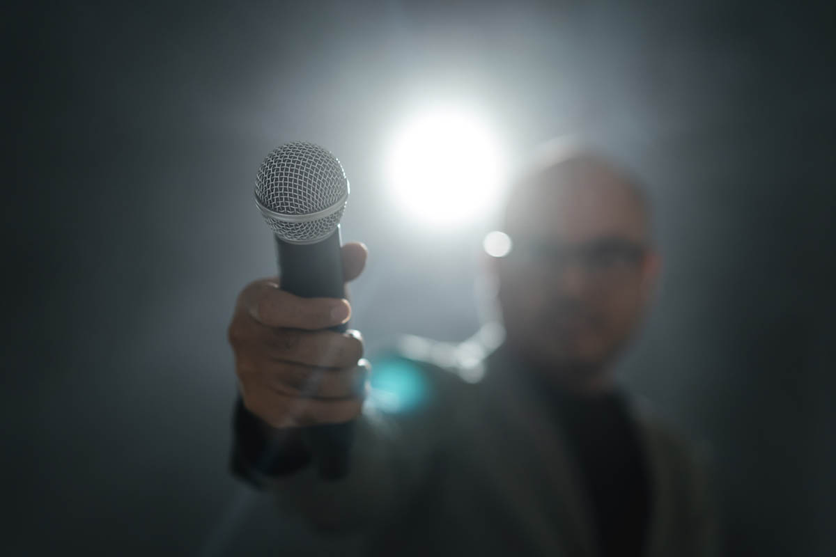 A man holds a microphone towards another person as a bright stage spotlight shines behind him, illustrating how shifting the spotlight and developing creative content marketing can capture attention.